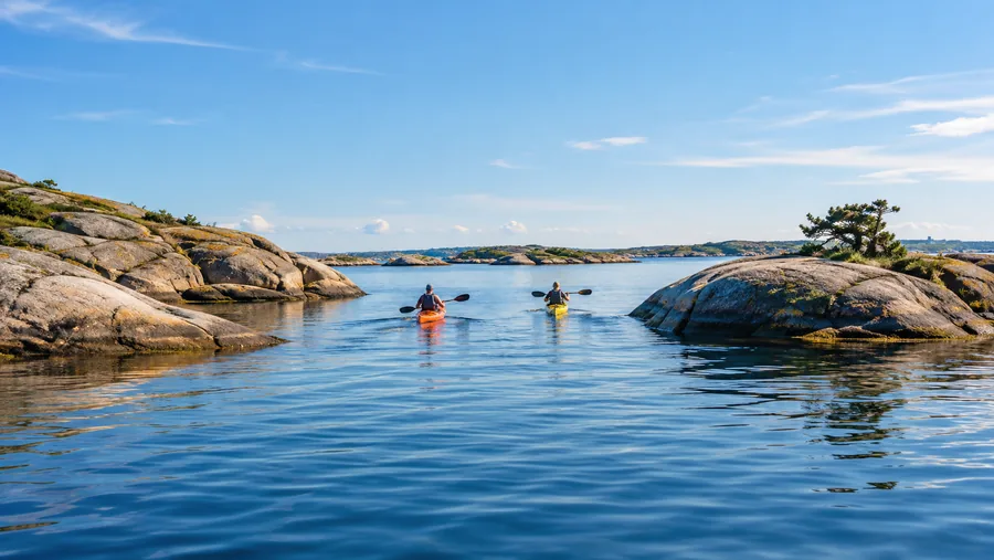 Två havskajaker, en orange och en gul, som paddlar mellan låga granitöar